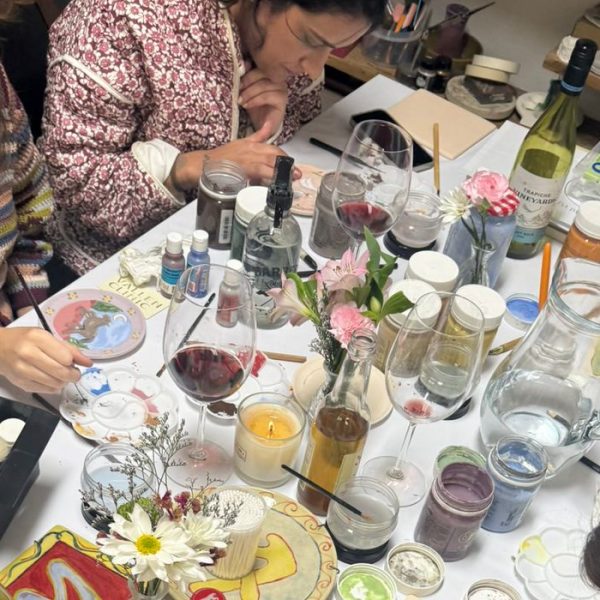 Mesa com tintas, flores, taças de vinho e pratos sendo pintados